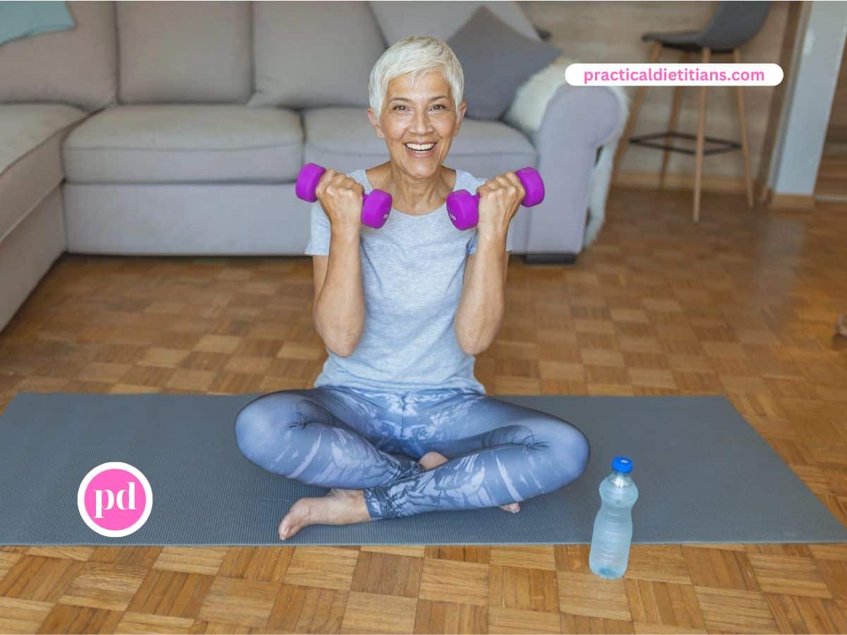 Woman seated on mat with legs crossed holding weights.