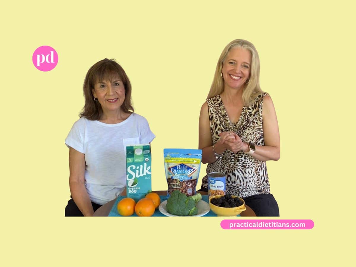 2 women showing oranges, soymilk, broccoli, almonds, blackberries, and pinto beans